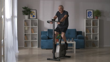 calm-sporty-middle-aged-man-is-training-on-spinning-bike-in-living-room-home-fitness-and-healthy-lifestyle-keeping-fit